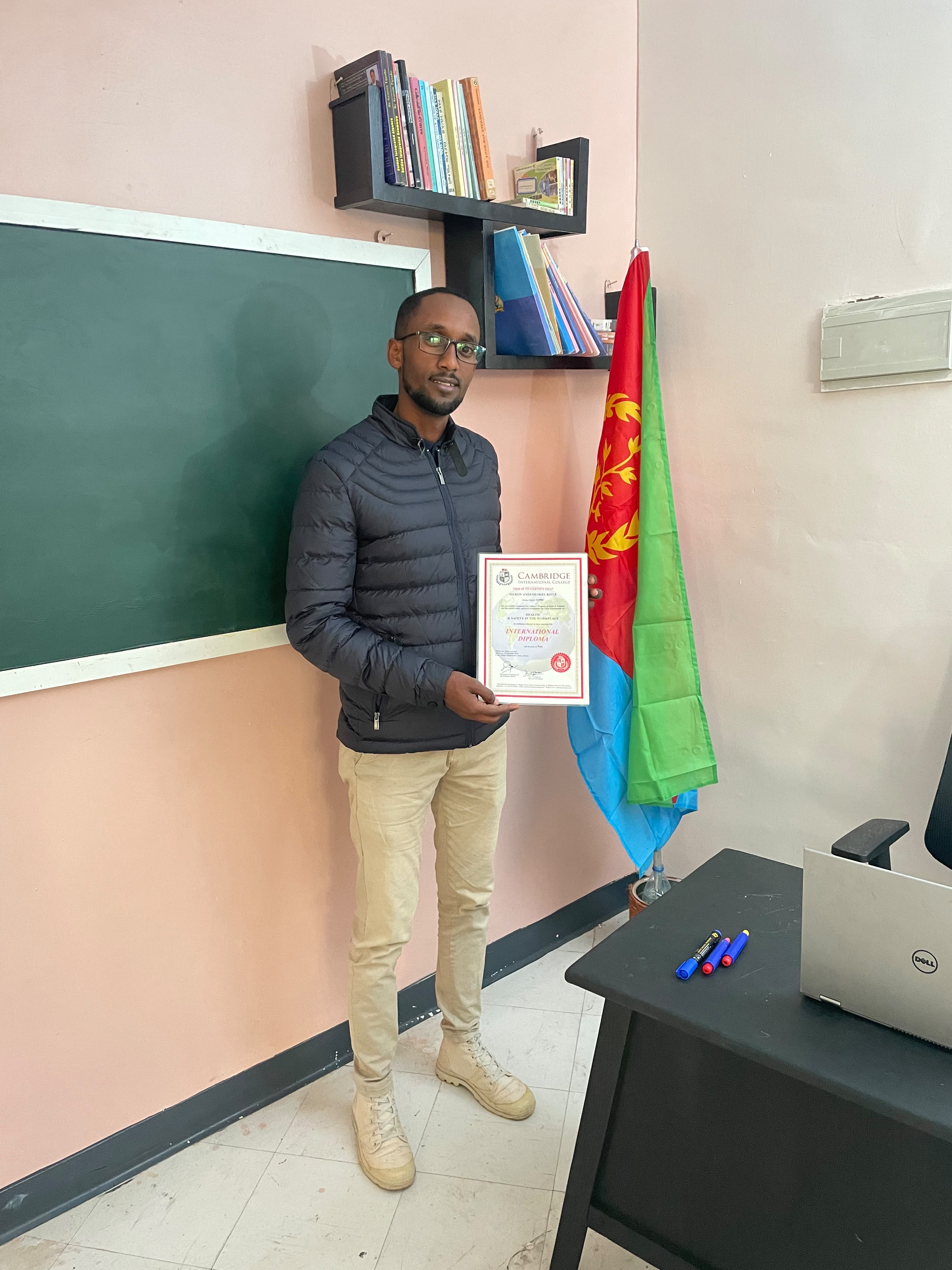 Graduate holding a Cambridge International College International Diploma beside the Eritrean flag